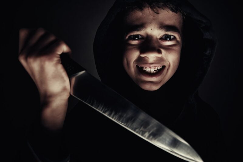 손에 칼을 든 까마귀를 입은 소년. 폭력적인 소년. 청소년 비행 개념