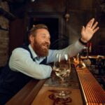 Happy smiling drunk man waving hand while sitting at bar counter